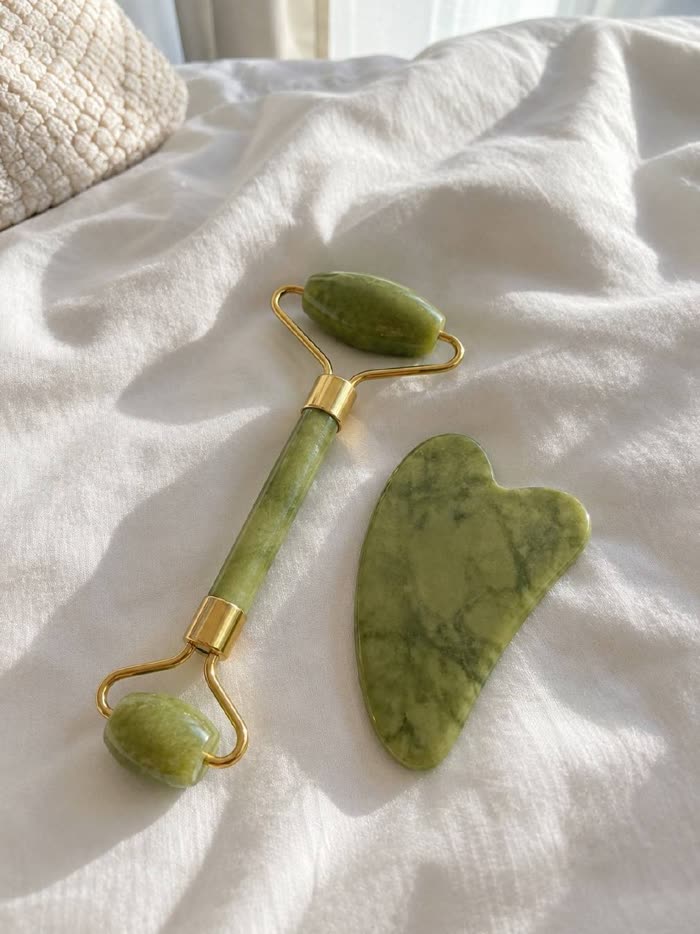 Roller de jade y gua sha sobre la ropa de cama blanca