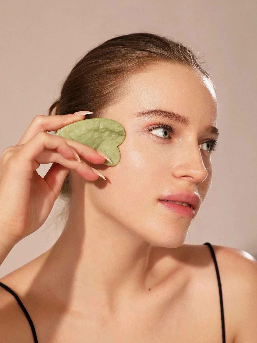 Mujer usando la gua sha de jade en el pómulo