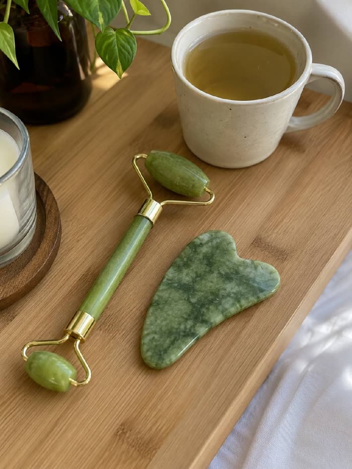 Roller de jade y gua sha en una bandeja de madera con una infusión y una vela