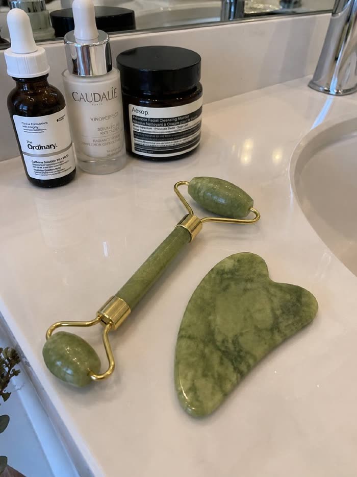 Roller y gua sha de jade con sérums y mascarilla en el baño